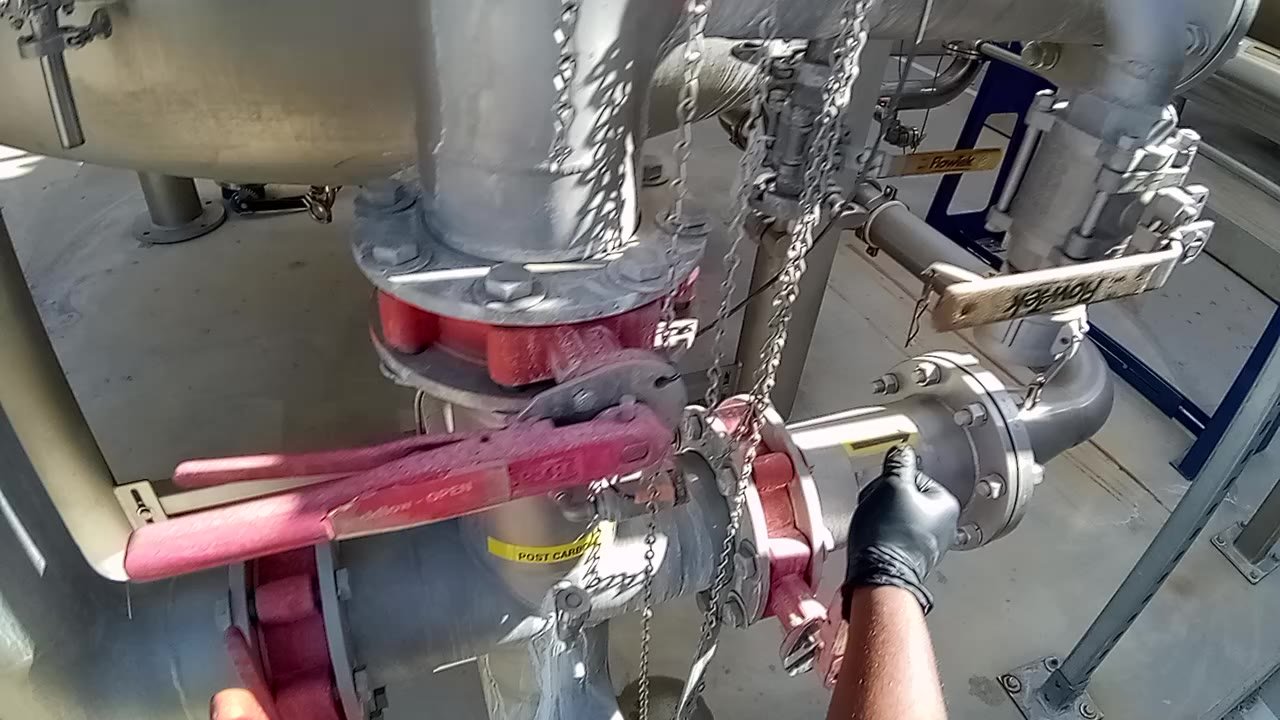 First-person view of a gloved hand closing a pipe valve during a plant procedure